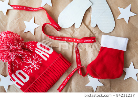 Red ribbon with the inscription Merry Christmas along with a red cap, mittens, red sock spread out on craft paper. Christmas celebration concept on December 25th. 94231237