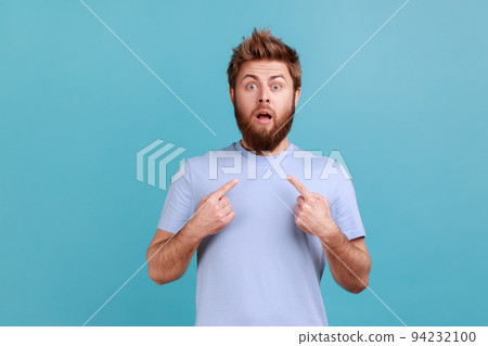 Wow, this is me. Portrait of astonished bearded man staring in amazement at camera and pointing herself, shocked by sudden success, can't believe. Indoor studio shot isolated on blue background. Wow, this is me. Portrait of astonished bearded man staring in amazement at camera and pointing herself, shocked by sudden success, can't believe. Indoor studio shot isolated on blue background. 94232100