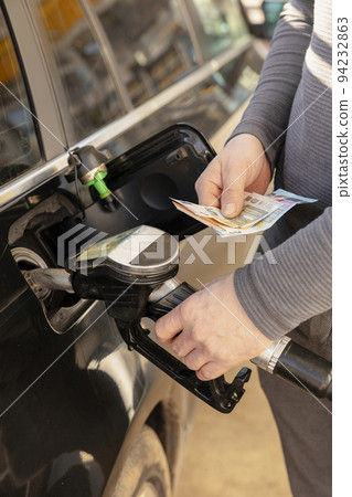 Car refuelling on petrol station. Man refilling car with fuel and holding money, euros. Close up. Gasoline, diesel is getting more expensive. Petrol industry and service. Petrol price and oil crisis. 94232863