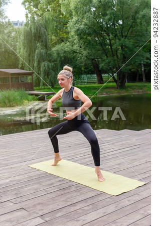 A slender woman on a wooden platform , does flow yoga in park in summer 94232887