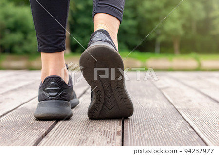 Close-up of women's legs in black sneakers walking on a wooden deck 94232977