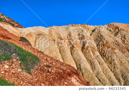 Details of the beautifully coloured cliffs on sunny day, clear blue sky. Yellow and red stone weathered slopes of Agios Ioannis beach, Milos, Greece Details of the beautifully coloured cliffs on sunny day, clear blue sky. Yellow and red stone weathered slopes of Agios Ioannis beach, Milos, Greece 94233345