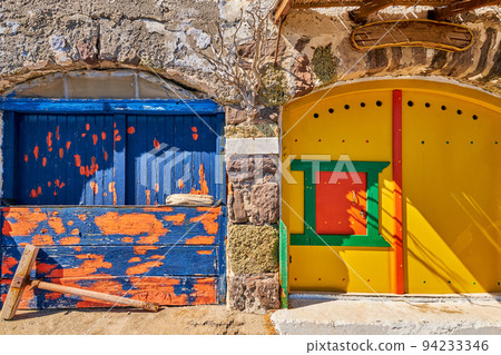 Colorful blue, yellow boat house doors, Klima fishermen village, Greece. Painted and weathered wooden doorways, whitewashed walls.  94233346