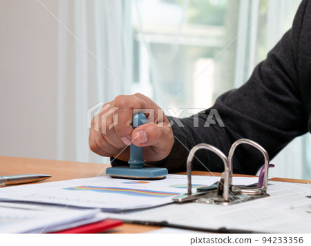 Close up Asian businessman holding rubber stamp and stamping with approved stamp Close up Asian businessman holding rubber stamp and stamping with approved stamp 94233356