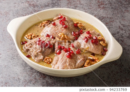 Fesenjan is a simple slowly cooked Iranian stew featuring ground walnuts, pomegranate molasses and chicken thighs close-up in a pan. Horizontal 94233769