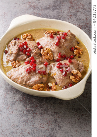 Fesenjan is an Iranian pomegranate and chicken stew made with ground walnuts, onions, squash, cinnamon, and pomegranate molasses close-up on the table. Vertical 94233772