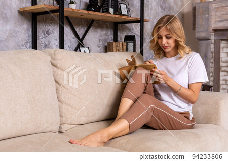 Thoughtful pensive woman sitting on sofa in modern white apartment, writing list to do in notepad using pen. 94233806