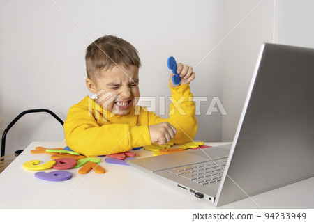 Little boy learning alphabet and numbers online, with laptop at home. Child is sad and stressed. Negative emotions, anger, stress, mental problems. Homeschooling and distance education for kids. 94233949