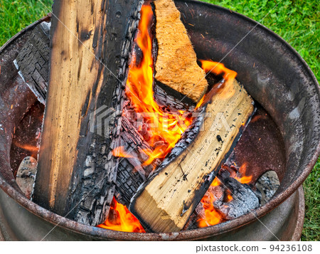 Campfire in a steel wheel on the concrete base and green lawn Campfire in a steel wheel on the concrete base and green lawn 94236108