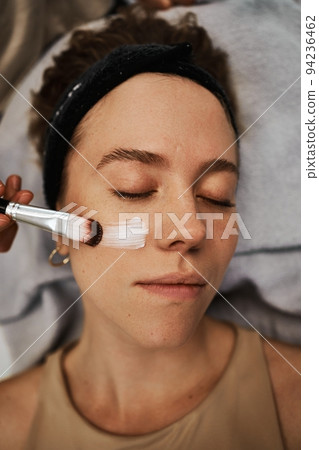 A smear of cream on the face of a young woman. Brush massage. 94236462