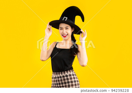 Young asian woman in black tank top wearing witch hat posing on yellow background for the halloween concept. 94239228
