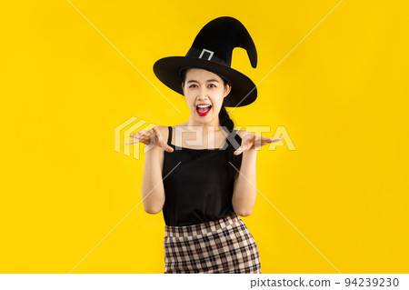 Young asian woman in black tank top wearing witch hat posing on yellow background for the halloween concept. Young asian woman in black tank top wearing witch hat posing on yellow background for the halloween concept. 94239230