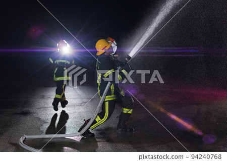 Firefighters use a water hose to eliminate a fire hazard. Team of firemen in the dangerous rescue mission. Firefighters use a water hose to eliminate a fire hazard. Team of firemen in the dangerous rescue mission. 94240768