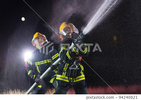 Firefighters using a water hose to eliminate a fire hazard. Team of female and male firemen in dangerous rescue mission.  94240821