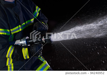 Firefighters use a water hose to eliminate a fire hazard. Team of firemen in the dangerous rescue mission. 94240952