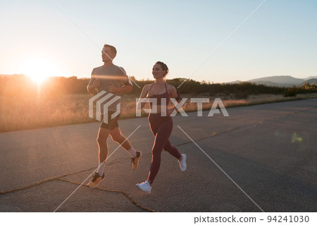 healthy young couple jogging in the city streets in the early morning with a beautiful sunrise in the background. healthy young couple jogging in the city streets in the early morning with a beautiful sunrise in the background. 94241030
