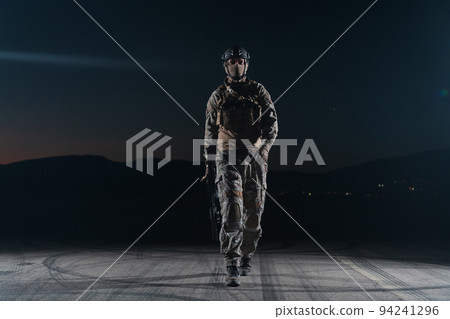 Army soldier in Combat Uniforms with an assault rifle, plate carrier and combat helmet going on a dangerous mission on a rainy night.  94241296