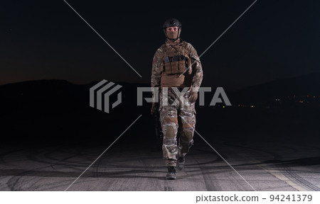 Army soldier in Combat Uniforms with an assault rifle, plate carrier and combat helmet going on a dangerous mission on a rainy night.  94241379