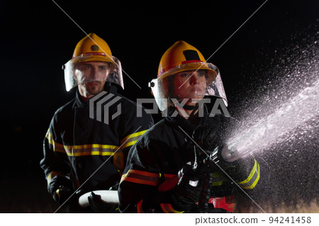 Firefighters using a water hose to eliminate a fire hazard. Team of female and male firemen in dangerous rescue mission.  94241458