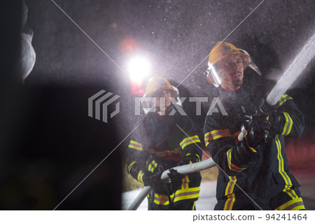 Firefighters using a water hose to eliminate a fire hazard. Team of female and male firemen in dangerous rescue mission.  94241464
