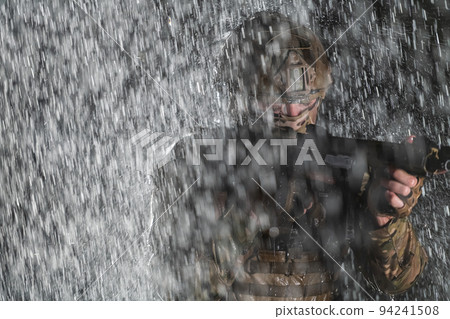 Army soldier in Combat Uniforms with an assault rifle, plate carrier and combat helmet going on a dangerous mission on a rainy night.  94241508