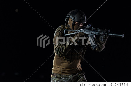Army soldier in Combat Uniforms with an assault rifle, plate carrier and combat helmet going on a dangerous mission on a rainy night.  94241714