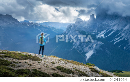 Girl with backpack on the hill looking at mountains at sunset Girl with backpack on the hill looking at mountains at sunset 94241934