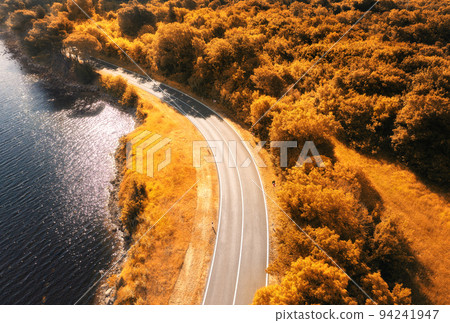 Aerial view of road near blue sea, forest at sunset in autumn Aerial view of road near blue sea, forest at sunset in autumn 94241947