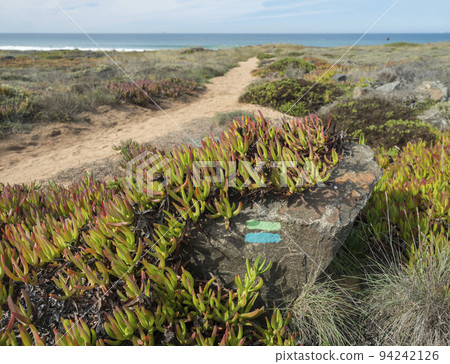 Stone with blue and green sign of Fishermans trail. Beautiful coastal hiking route that mixes sandy beaches, sea cliffs and vegetation. Porto Covo, Portugal 94242126