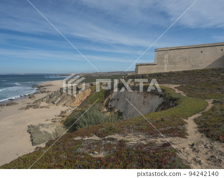 View of wall of fortress at Praia da Ilha do Pessegueiro sand beach with ocean waves at Rota Vicentina coast near Porto Covo, Portugal. 94242140
