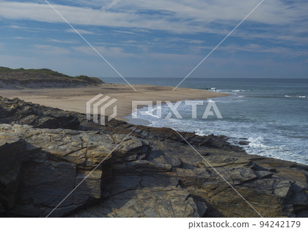View of empty Praia do Sissal sand beach with ocean waves and sharp rock and cllifs at wild Rota Vicentina coast near Porto Covo, Portugal. 94242179