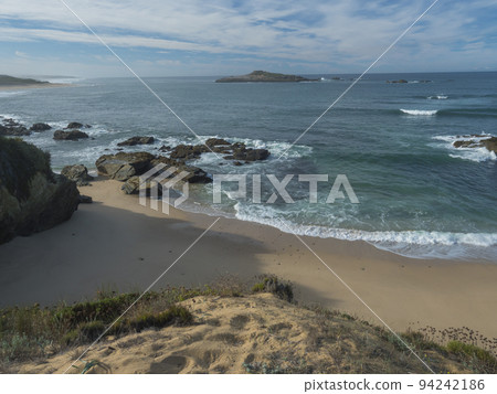 View of empty Praia do Sissal sand beach with ocean waves and sharp rock and cllifs at wild Rota Vicentina coast near Porto Covo, Portugal. 94242186