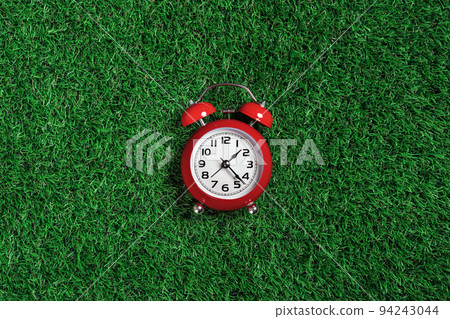 red alarm clock on turf green grass background red alarm clock on turf green grass background 94243044