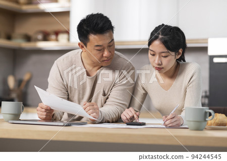 Asian spouses counting monthly expenses, kitchen interior 94244545