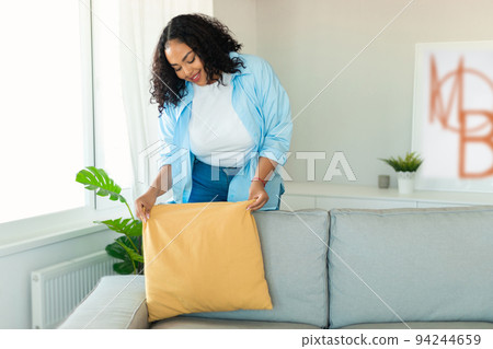 African Woman Decorating Room Putting Pillow On Couch At Home African Woman Decorating Room Putting Pillow On Couch At Home 94244659