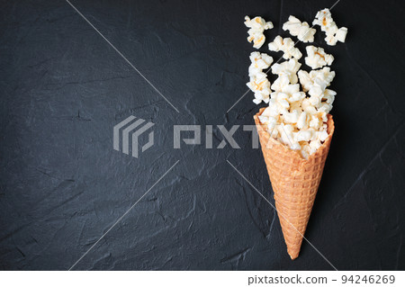 Waffle Cone with Salted Popcorn on black concrete background. Snack concept Waffle Cone with Salted Popcorn on black concrete background. Snack concept 94246269