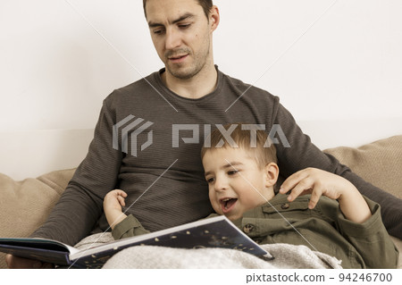 Father and son reading a book on the bed at home. Young attractive man and little boy resting in bedroom. Natural earth colors. Cozy environment. Father reads a fairy tale for his child. Father and son reading a book on the bed at home. Young attractive man and little boy resting in bedroom. Natural earth colors. Cozy environment. Father reads a fairy tale for his child. 94246700