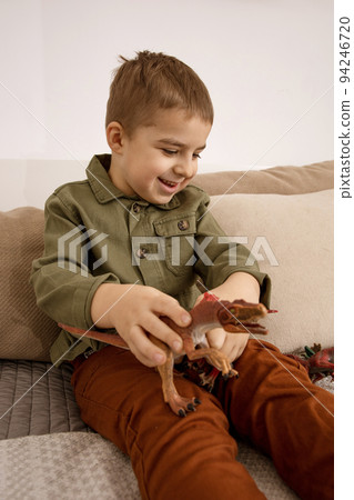 Little and cute caucasian boy playing with dinosaurs at home. Interior and clothes in natural earth colors. Cozy environment. Child having fun with toys. Little and cute caucasian boy playing with dinosaurs at home. Interior and clothes in natural earth colors. Cozy environment. Child having fun with toys. 94246720