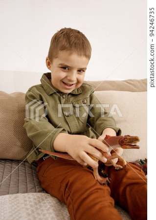 Little and cute caucasian boy playing with dinosaurs at home. Interior and clothes in natural earth colors. Cozy environment. Child having fun with toys. Little and cute caucasian boy playing with dinosaurs at home. Interior and clothes in natural earth colors. Cozy environment. Child having fun with toys. 94246735