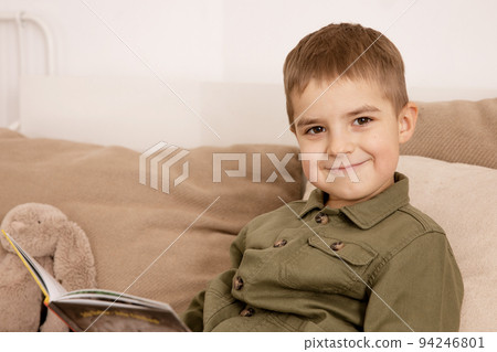 Little and cute caucasian boy reading a book on the bed at home. Interior and clothes in natural earth colors. Cozy environment. Child reads a fairy tale. Little and cute caucasian boy reading a book on the bed at home. Interior and clothes in natural earth colors. Cozy environment. Child reads a fairy tale. 94246801