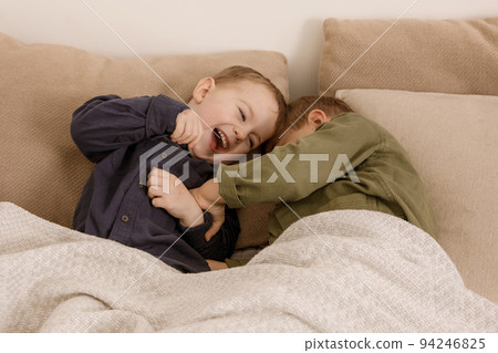Two little and cute caucasian boys playing together on the bed at home. Interior and clothes in natural earth colors. Cozy environment. Children having fun, two brothers kittle each other. 94246825
