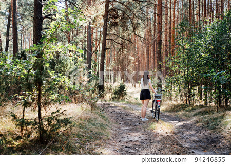 Mental health benefits of cycling, reduce anxiety. Cycling in forest. Forest Bycycle Trails. Single woman riding bike in pine forest in sunny day. Mental health benefits of cycling, reduce anxiety. Cycling in forest. Forest Bycycle Trails. Single woman riding bike in pine forest in sunny day. 94246855
