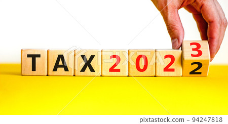 2023 tax new year symbol. Businessman turns a wooden cube and changes words Tax 2022 to Tax 2023. Beautiful yellow table white background, copy space. Business 2023 tax new year concept. 2023 tax new year symbol. Businessman turns a wooden cube and changes words Tax 2022 to Tax 2023. Beautiful yellow table white background, copy space. Business 2023 tax new year concept. 94247818