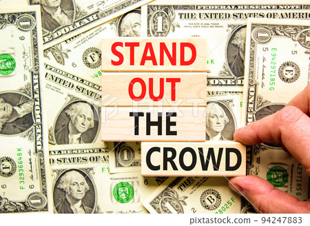 Stand out the crowd symbol. Concept words Stand out the crowd on wooden blocks on beautiful background from dollar bills. Businessman hand. Business, stand out the crowd concept 94247883