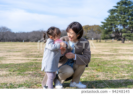 Kindergarteners and nursery teachers playing on the lawn square in the park 94248145