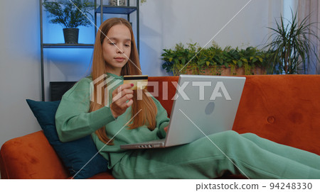Young teen girl using credit bank card and laptop, transferring money, purchases online shopping Young teen girl using credit bank card and laptop, transferring money, purchases online shopping 94248330
