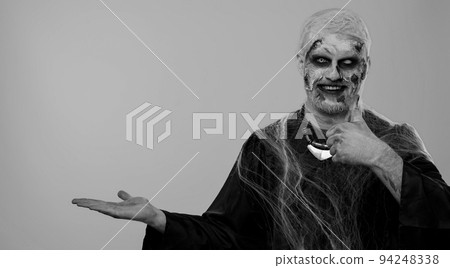 Scary wounded Halloween zombie undead man showing thumbs up and pointing at right on blank space 94248338