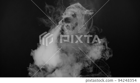 Frightening man Halloween zombie bloody wounded hiding behind hands blows smoke from nose and mouth Frightening man Halloween zombie bloody wounded hiding behind hands blows smoke from nose and mouth 94248354