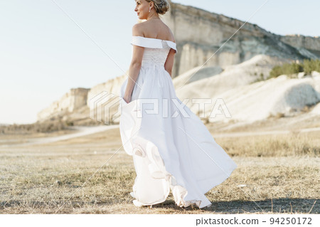 Back view of a bride in a white dress with bare shoulders standing in a field 94250172
