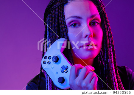 Young woman with long braids holding console joystick against dark purple background 94250596